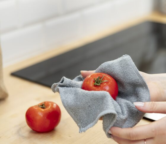 Mains qui essuient une tomate avec un essuie-tout lavable.