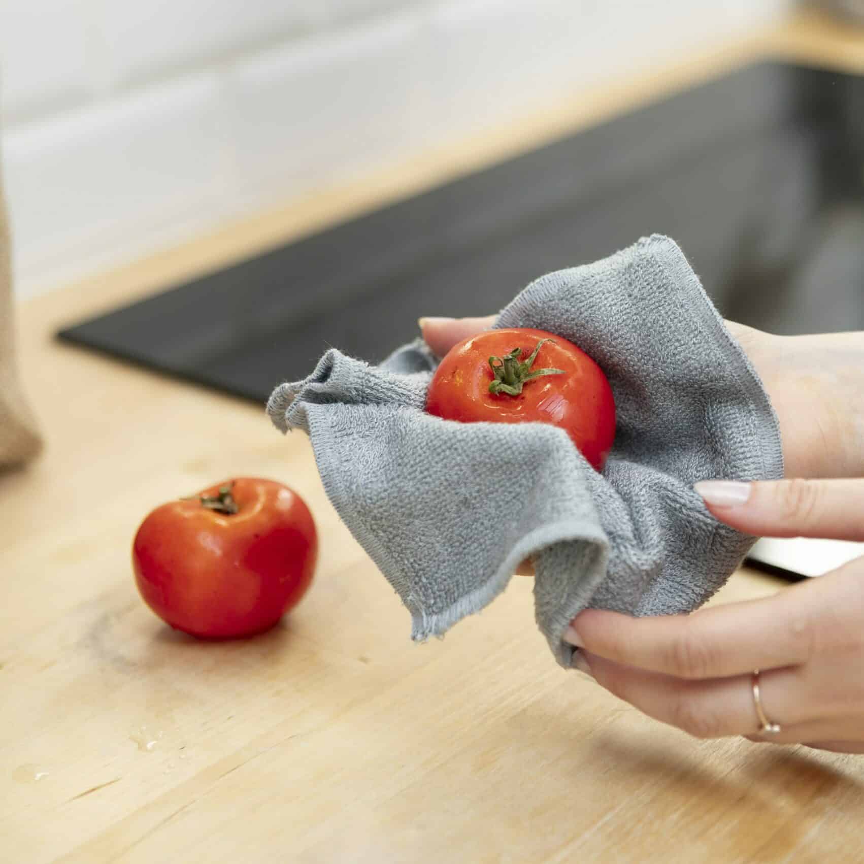 Mains qui essuient une tomate avec un essuie-tout lavable.