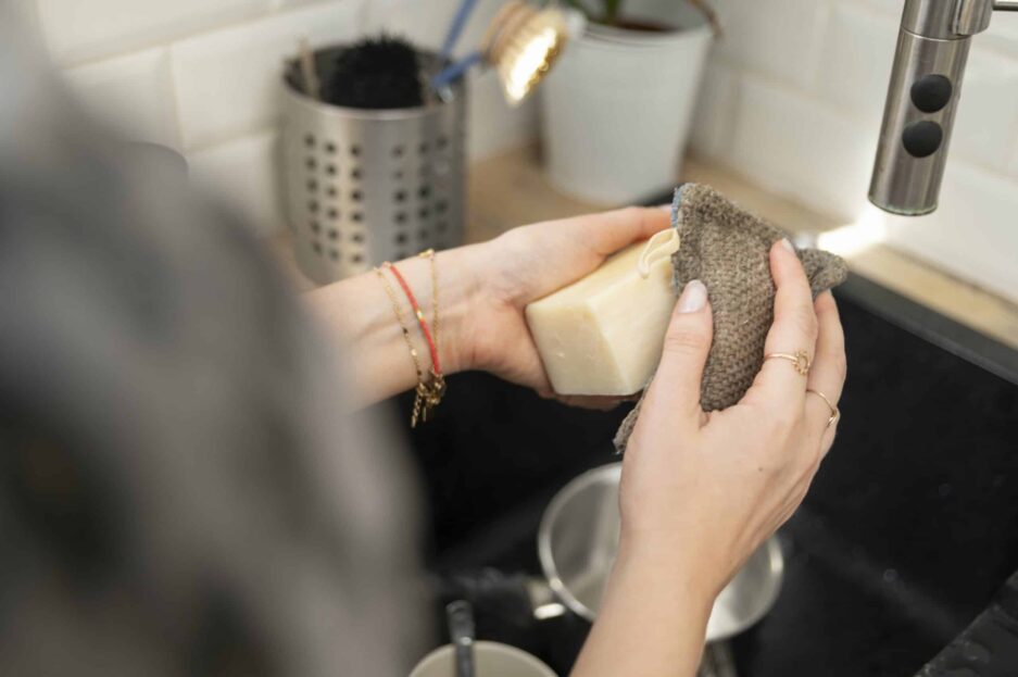 Femme qui fait la vaisselle avec un savon vaisselle solide et une éponge lavable.