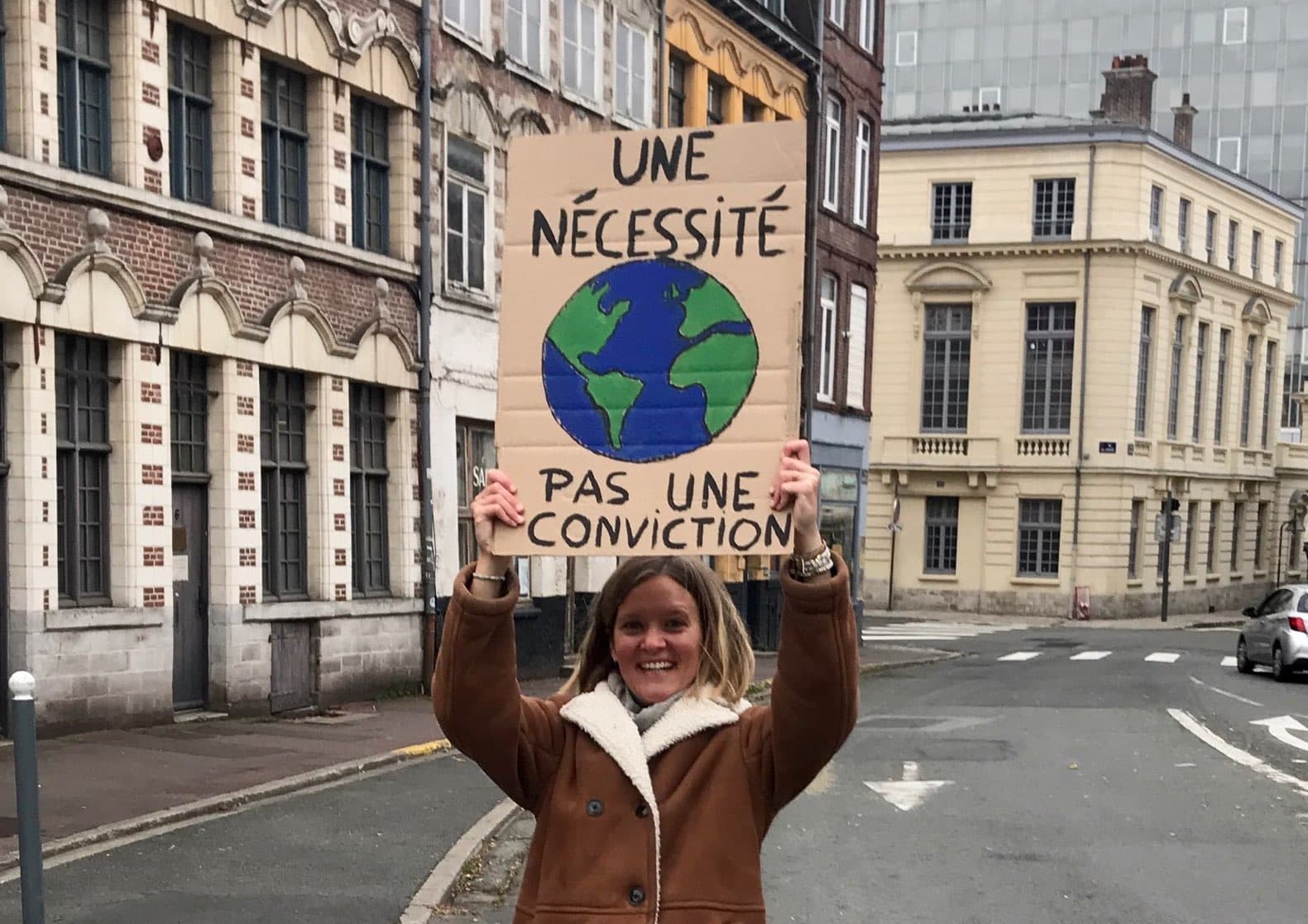 Femme qui tient un panneau : "une nécessité, pas une conviction".