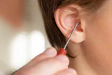 Main d'adulte qui met un cure-oreille dans l'oreille d'un enfant.