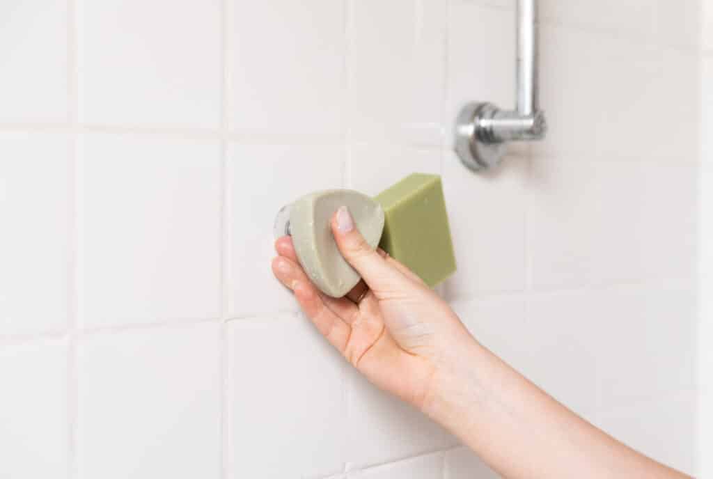 savon solide et shampoing solide accrochés sur un mur de salle de bain avec un porte-savon magnétique